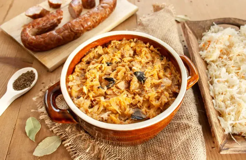 Bigos w glinianym naczyniu i kiełbasa na desce